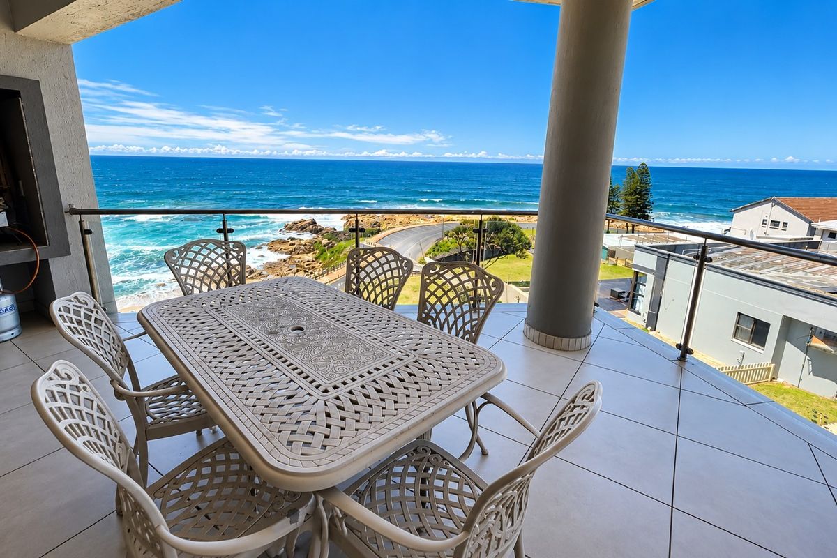 Spacious covered balcony featuring a built-in braai, modern glass balustrade, and expansive ocean views, perfect for outdoor entertaining.