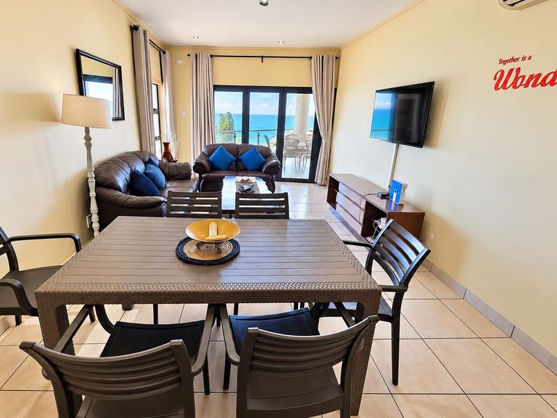 Open plan living and dining area featuring tiled flooring, air conditioning, and sliding glass doors leading to a balcony with ocean views.