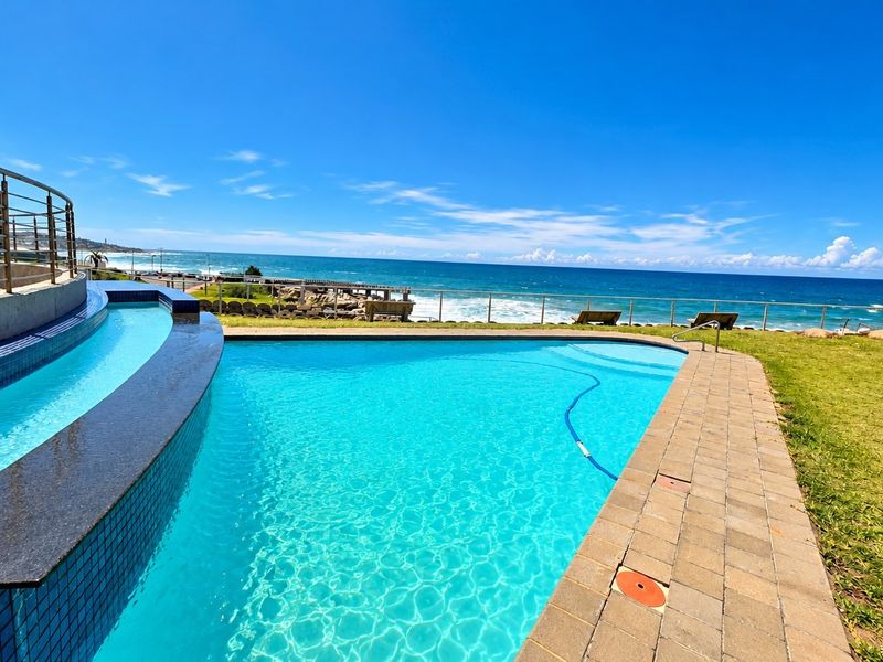 A well-maintained swimming pool area featuring a modern tiled edge, metal balustrades, and expansive ocean views.