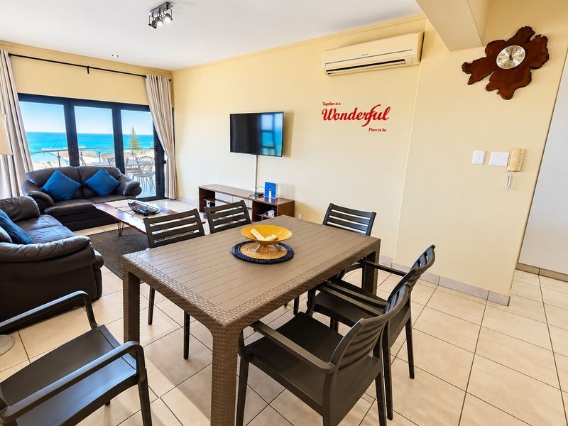 Open-plan living and dining area featuring tiled floors, split-system air conditioning, and large sliding doors opening to a balcony with ocean views.
