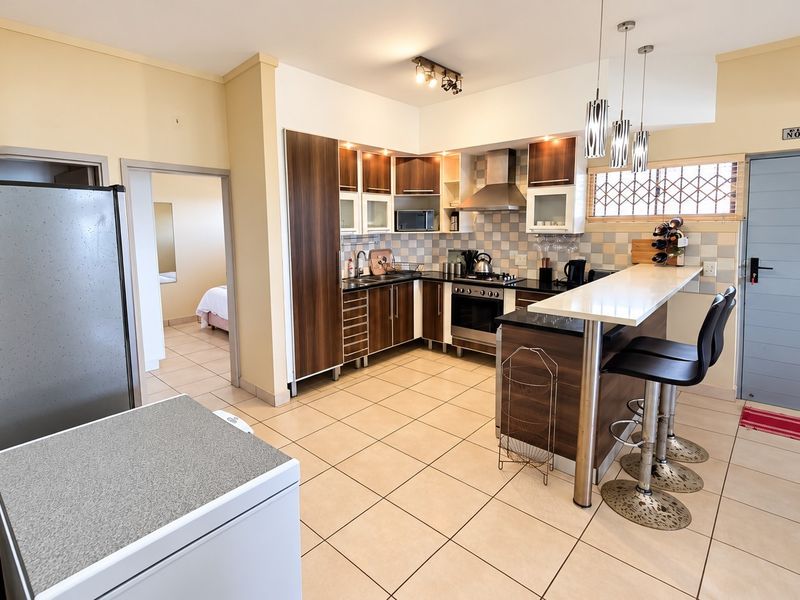 Open plan kitchen featuring dark wood cabinetry, granite countertops, a breakfast bar, and tiled flooring, seamlessly connecting to the living area.