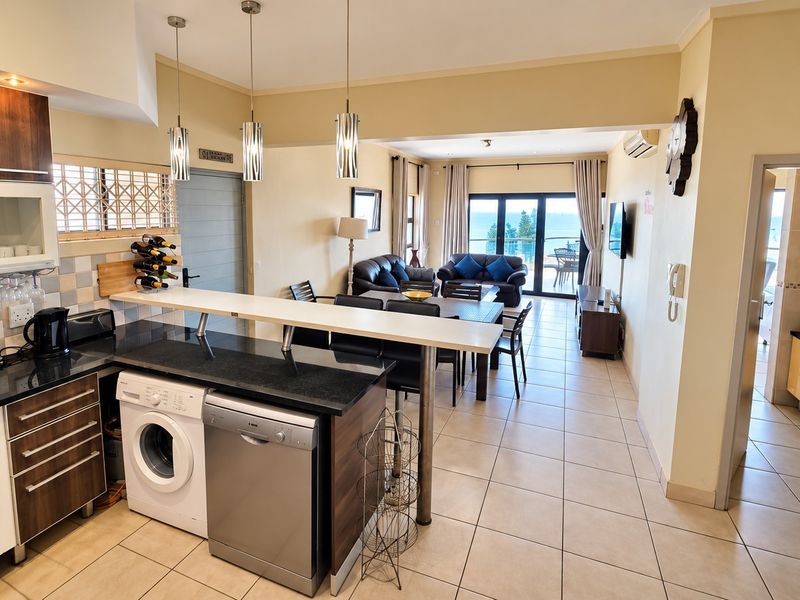 Spacious open-plan kitchen and living area featuring tiled floors, modern cabinetry, integrated appliances, and seamless access to a balcony with ocean views.