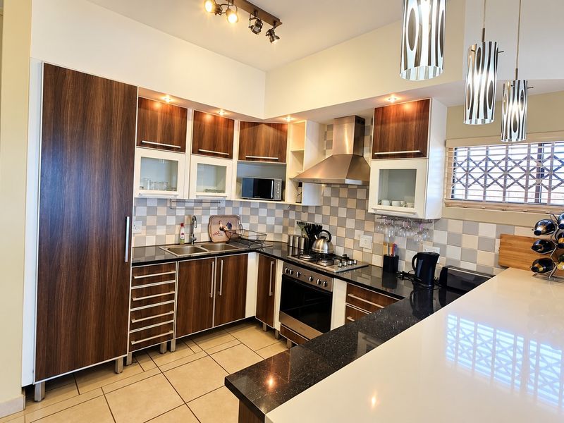 A well-maintained kitchen featuring dark wood cabinetry, granite countertops, a stainless steel extractor fan, and a gas hob with a tiled backsplash.