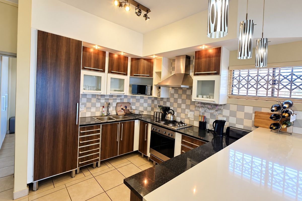 A well-maintained kitchen featuring dark wood cabinetry, granite countertops, a stainless steel extractor fan, and a gas hob with a tiled backsplash.