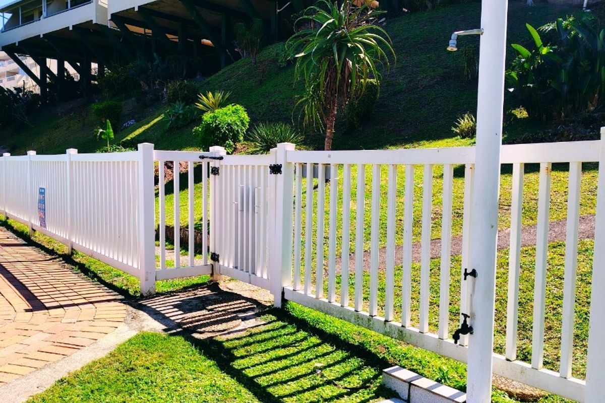 Exterior view of the apartment complex grounds featuring a well-maintained outdoor shower area with a tiled base and white picket fencing.