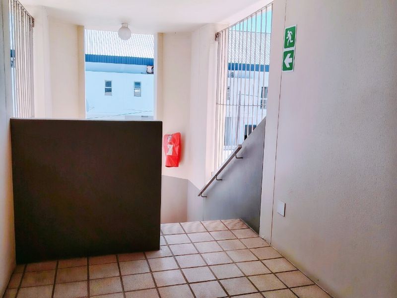 A functional apartment building hallway featuring tiled flooring, a staircase with a handrail, and essential safety equipment including a fire extinguisher and exit signage.