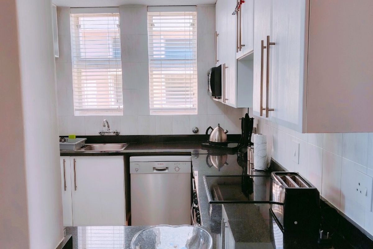 A functional kitchen featuring dark granite countertops, white cabinetry, tiled backsplash, and integrated dishwasher, illuminated by modern ceiling spotlights.