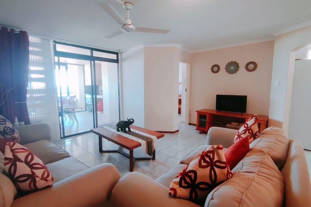 A comfortable living room featuring tiled flooring, a ceiling fan, and large sliding glass doors that provide access to an outdoor patio area.