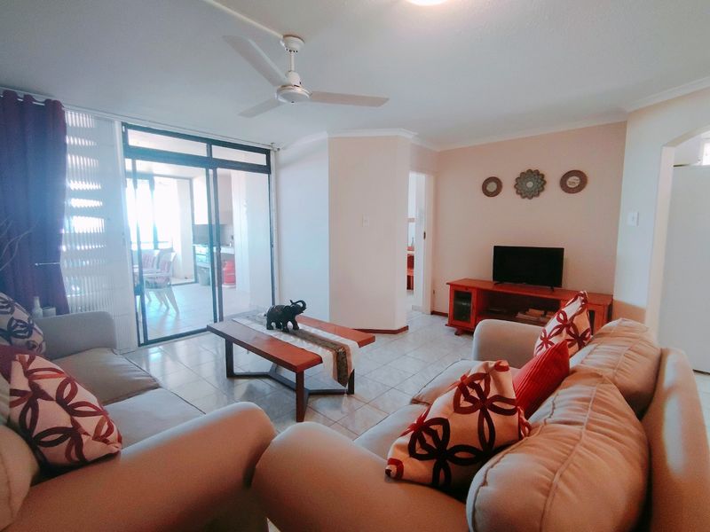 A comfortable living room featuring tiled flooring, a ceiling fan, and large sliding glass doors that provide access to an outdoor patio area.