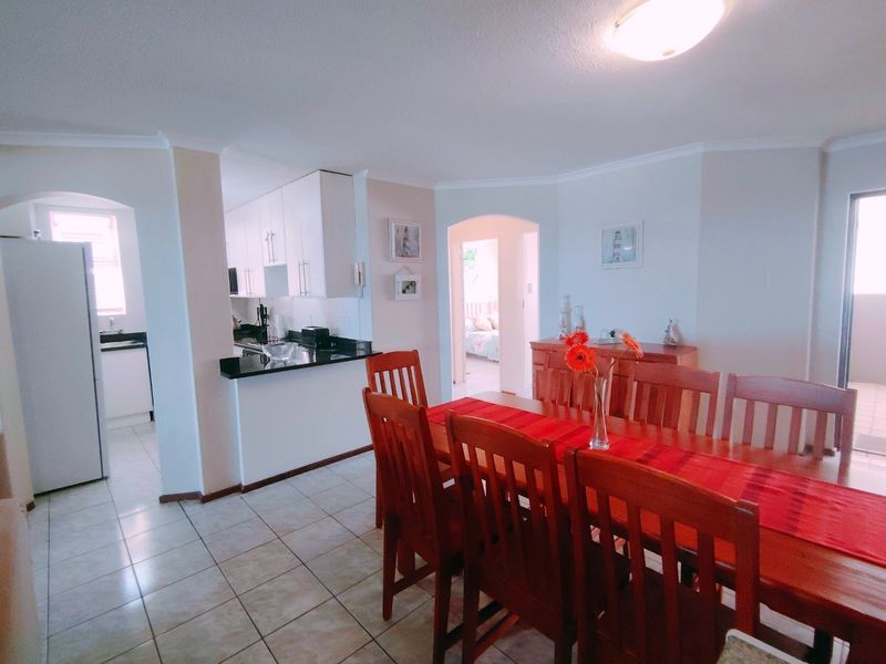 Open plan dining area featuring tiled flooring and an adjacent kitchen with granite countertops and white cabinetry.