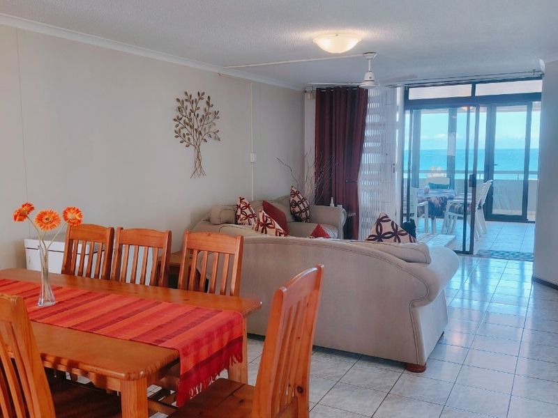 Open plan living and dining area featuring tiled flooring, ceiling fan, and large sliding glass doors leading to a balcony with ocean views.