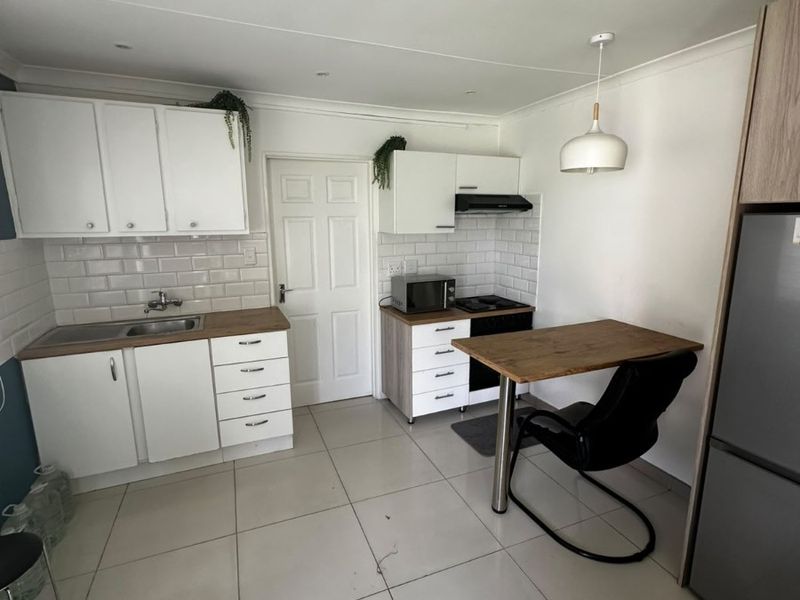 A functional kitchen featuring white cabinetry, subway tile backsplash, stainless steel sink, built-in hob with extractor fan, and tiled flooring.