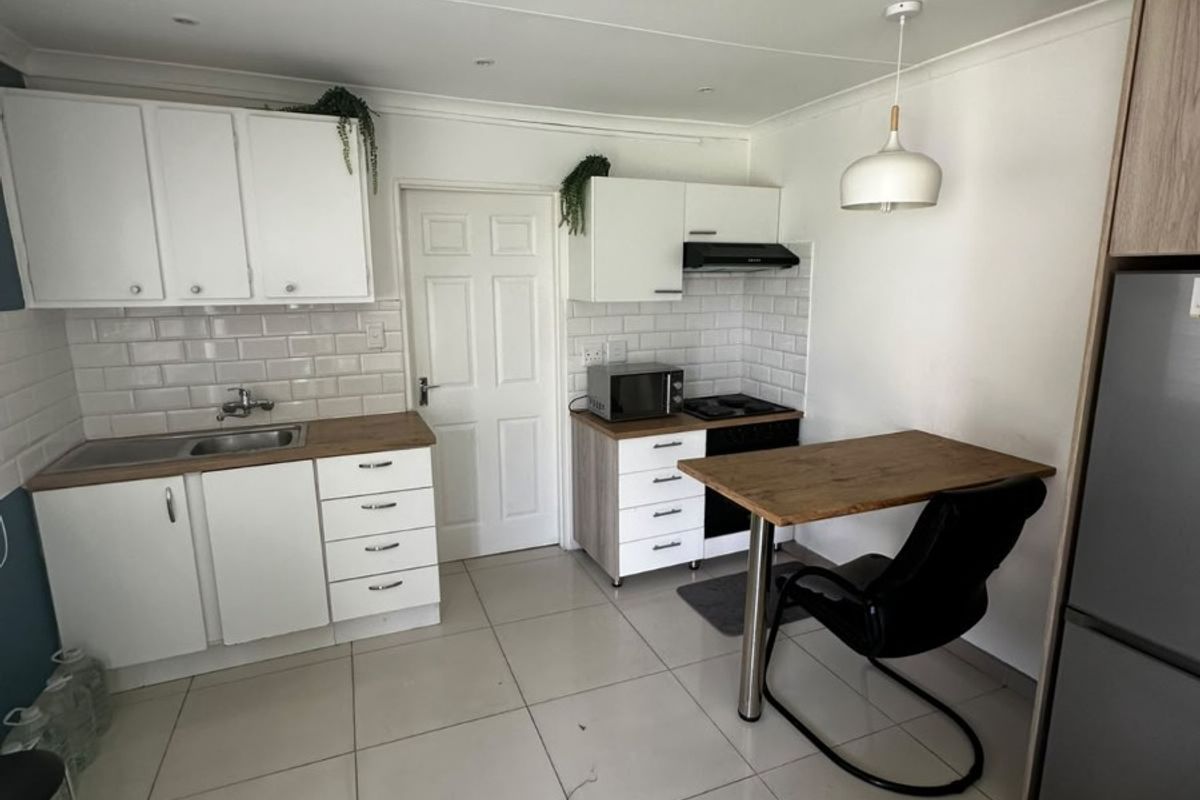 A functional kitchen featuring white cabinetry, subway tile backsplash, stainless steel sink, built-in hob with extractor fan, and tiled flooring.