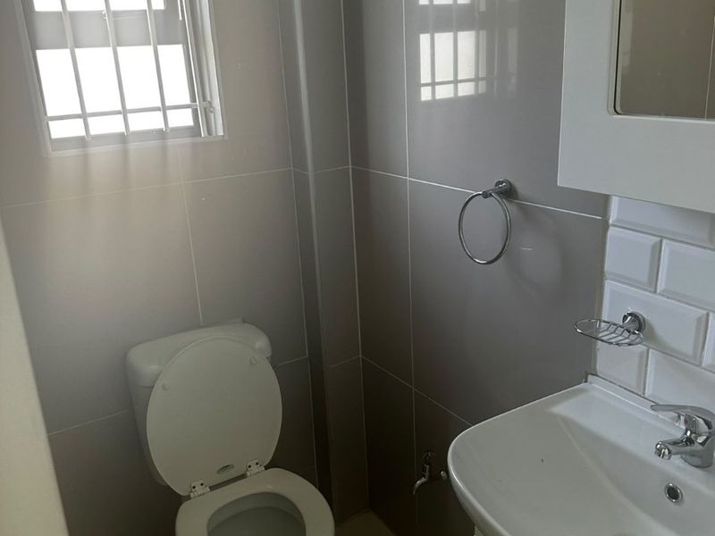 A clean, modern bathroom featuring tiled walls, a vanity basin, and a toilet, with a window fitted with security bars.