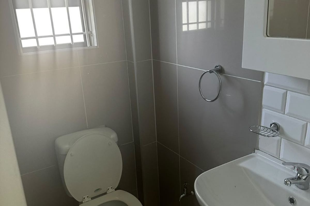 A clean, modern bathroom featuring tiled walls, a vanity basin, and a toilet, with a window fitted with security bars.
