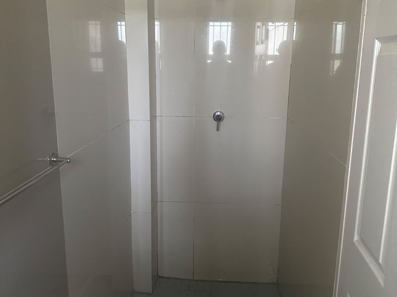 A functional shower stall featuring tiled walls and flooring, equipped with a standard shower head and mixer tap.