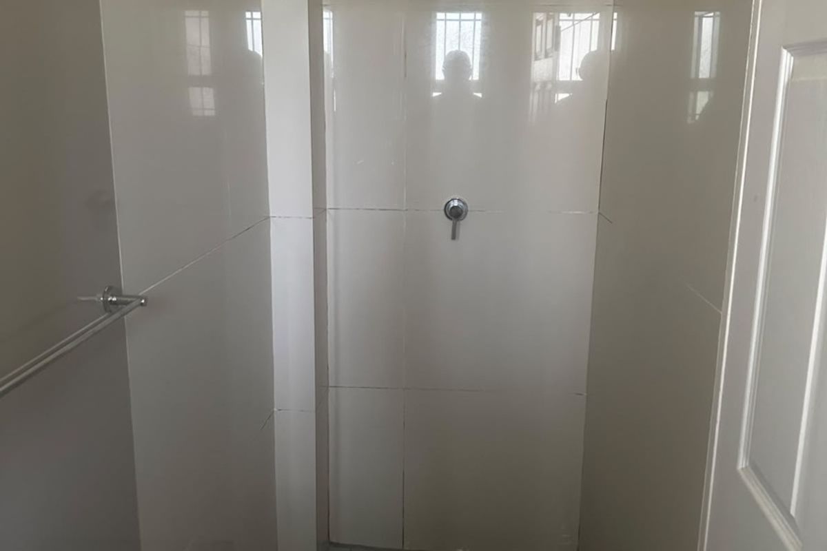 A functional shower stall featuring tiled walls and flooring, equipped with a standard shower head and mixer tap.
