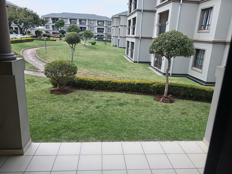 A view from a tiled patio overlooking a well-maintained communal garden and apartment complex grounds.