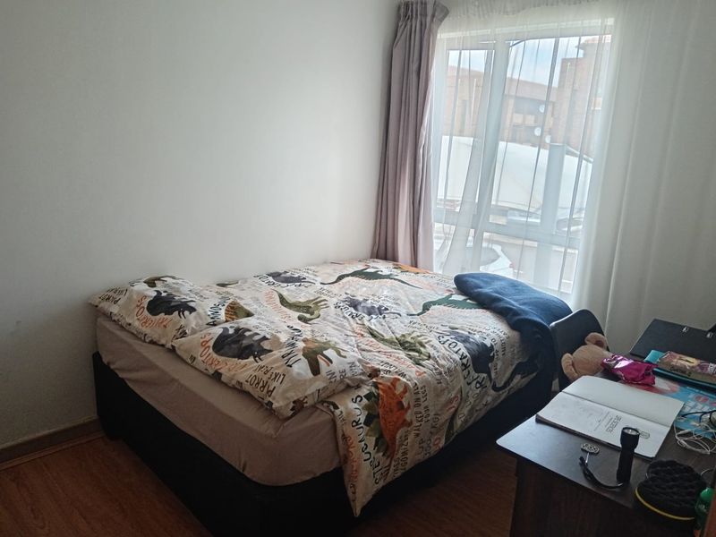A functional bedroom featuring laminate flooring and large windows with curtain tracks, providing natural light.