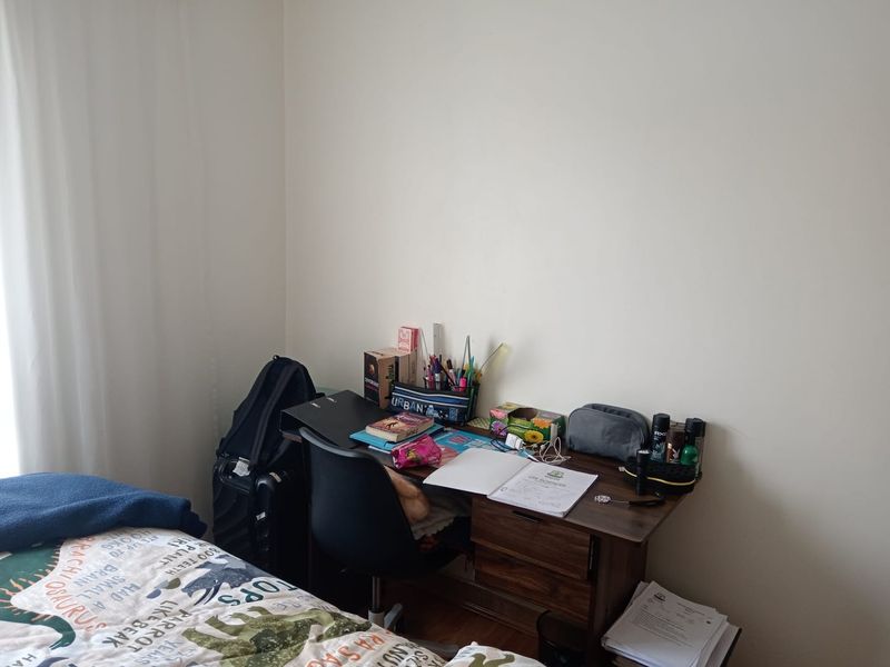A bedroom corner featuring plain walls and neutral flooring, currently utilized as a study area.