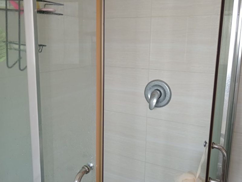 A functional shower enclosure featuring tiled walls, a standard shower mixer, and glass doors.