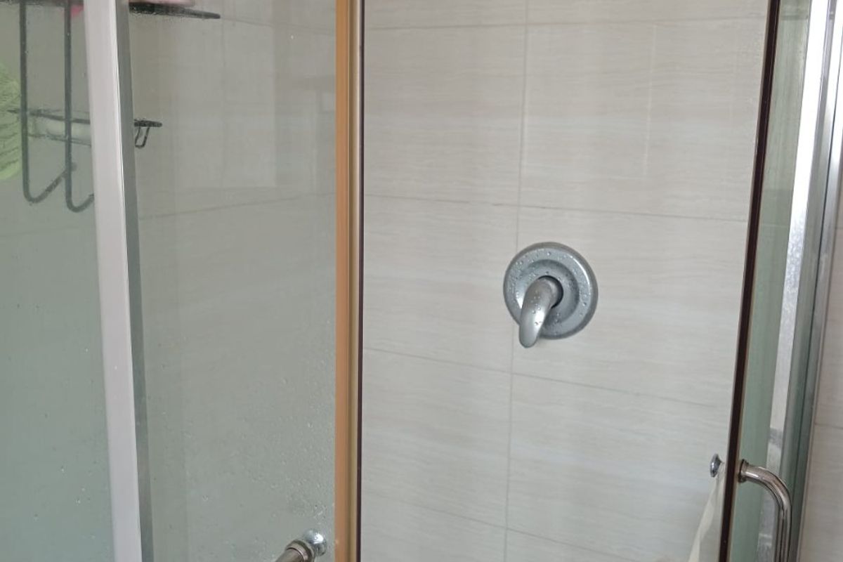 A functional shower enclosure featuring tiled walls, a standard shower mixer, and glass doors.