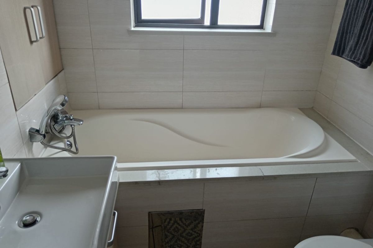 A functional bathroom featuring a built-in bathtub with shower mixer, wall-mounted basin, and neutral tiled finishes throughout.