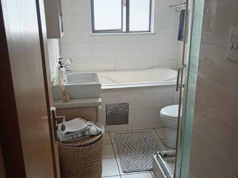 A functional bathroom featuring a built-in bathtub, separate shower enclosure, and a vanity basin with tiled finishes throughout.
