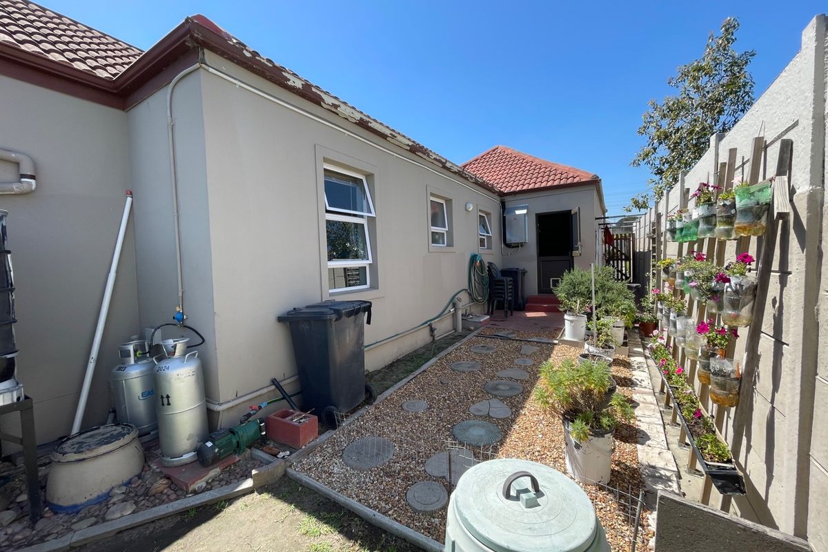 Rear exterior view of the property featuring a gravel pathway, tiled roof, and boundary wall with vertical garden elements.