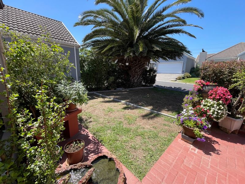 A private garden area featuring brick paving, a small lawn, and mature landscaping, adjacent to the property's garage and main structure.