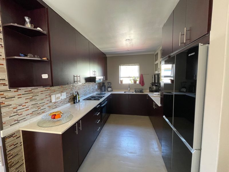 A functional galley-style kitchen featuring dark wood cabinetry, stone countertops, a mosaic tile backsplash, and integrated appliances.