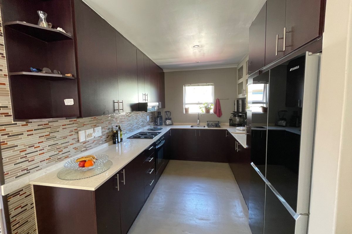 A functional galley-style kitchen featuring dark wood cabinetry, stone countertops, a mosaic tile backsplash, and integrated appliances.