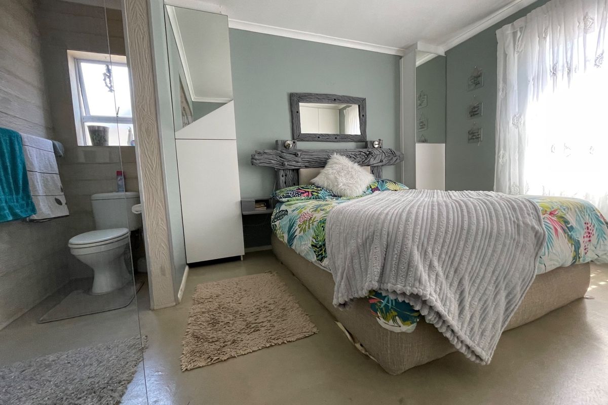A bedroom featuring an open-plan en-suite bathroom with a toilet, built-in cupboards with mirrored doors, and neutral tiled flooring.