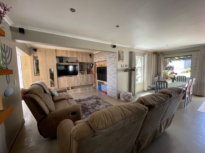 Spacious open-plan living and dining area featuring polished concrete floors, custom built-in cabinetry, a stone-clad feature wall, and large sliding doors leading outdoors.