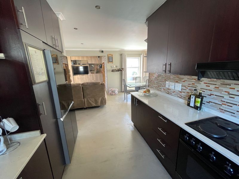 Open-plan kitchen and living area featuring dark cabinetry, stone countertops, mosaic backsplash, and integrated appliances, creating a functional and connected living space.