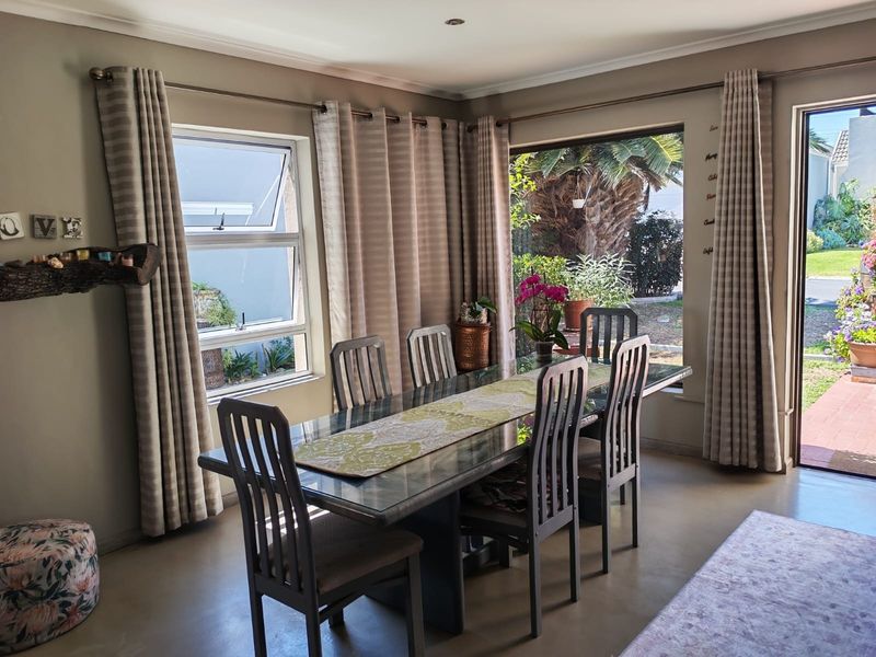 A bright dining room featuring large aluminium windows and a sliding door providing natural light and direct access to the garden area.