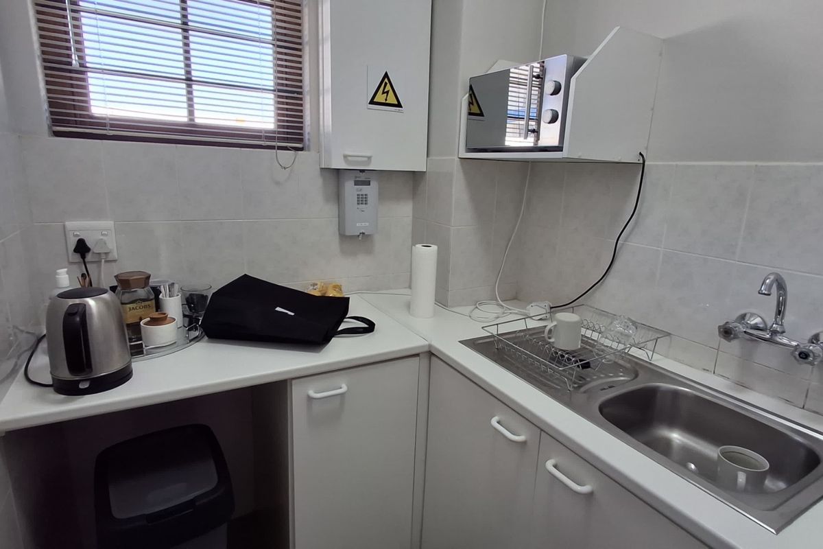 A compact office kitchenette featuring a stainless steel sink, tiled backsplash, and built-in cabinetry with laminate countertops.