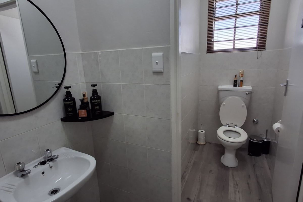 A clean and functional bathroom featuring a ceramic washbasin, a standard toilet, tiled wall finishes, and wood-look laminate flooring.
