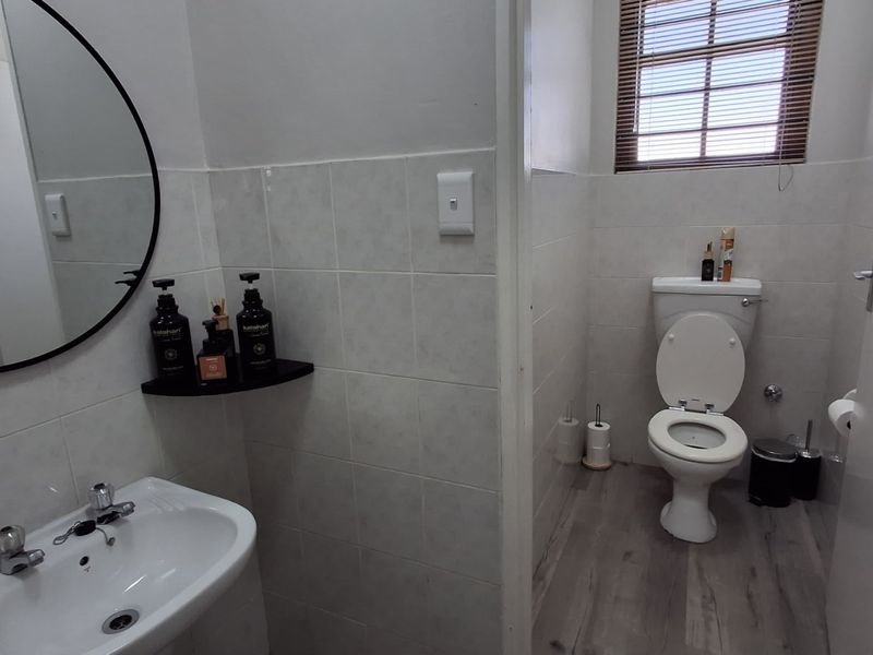 A clean and functional bathroom featuring a ceramic washbasin, a standard toilet, tiled wall finishes, and wood-look laminate flooring.