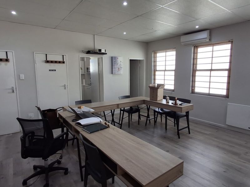 A functional office space featuring laminate flooring, recessed lighting, a split-system air conditioner, and multiple windows with venetian blinds.