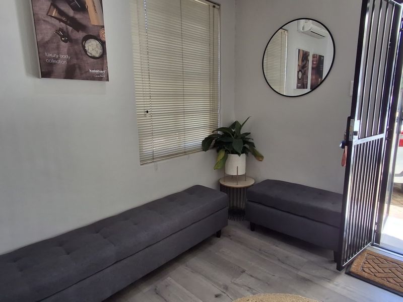 A bright and welcoming office entrance area featuring laminate flooring, venetian blinds, and a secure metal entrance gate.