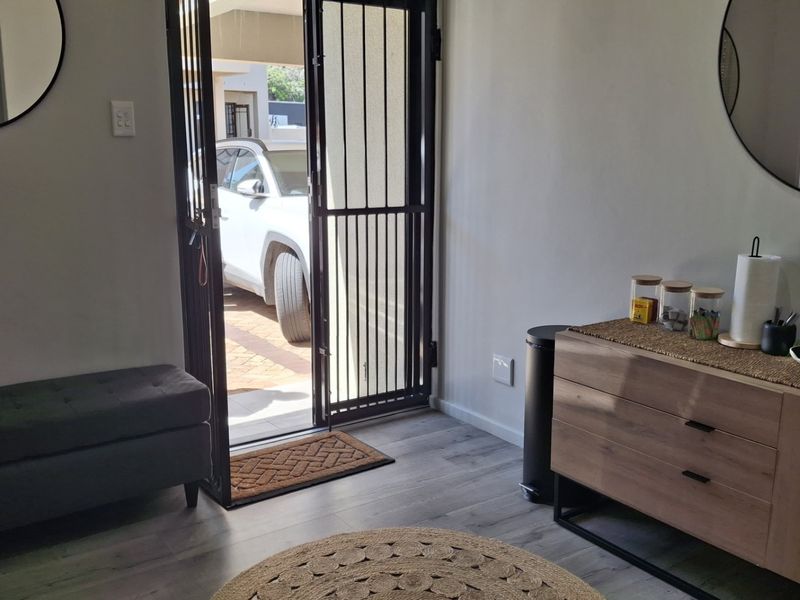 A bright office entry area featuring modern laminate flooring and a secure metal entrance gate leading to the exterior.