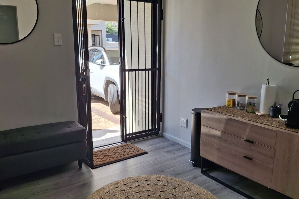 A bright office entry area featuring modern laminate flooring and a secure metal entrance gate leading to the exterior.