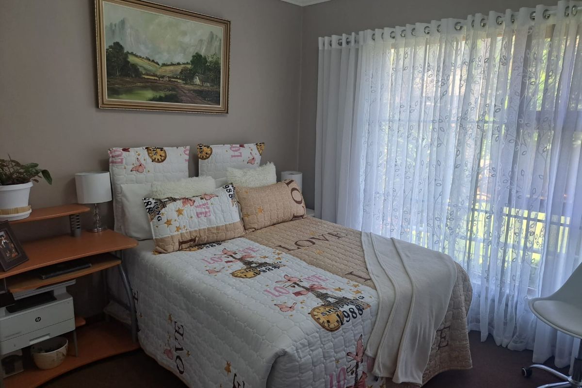 A cozy bedroom featuring neutral wall tones, carpeted flooring, and large windows dressed with sheer curtains, providing ample natural light.