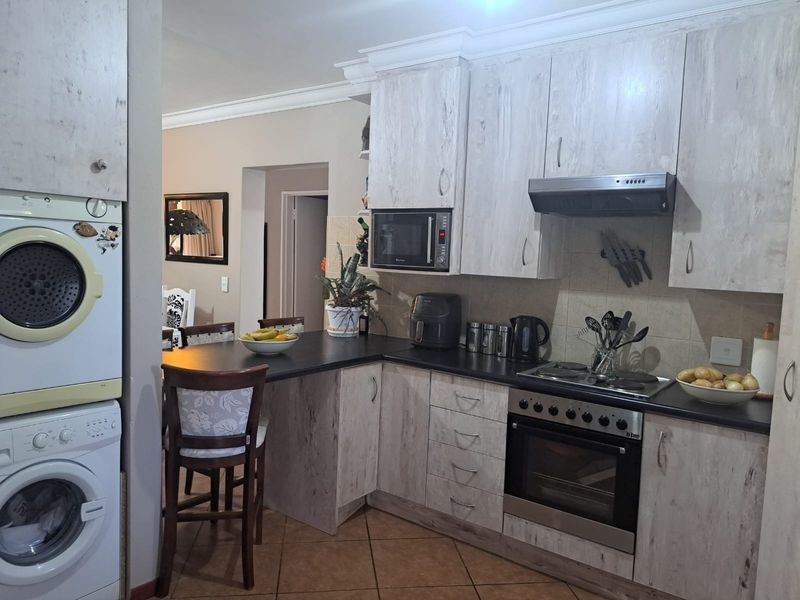 A functional kitchen featuring light wood-grain cabinetry, dark countertops, built-in oven and hob, and a dedicated laundry area with stacked appliances.