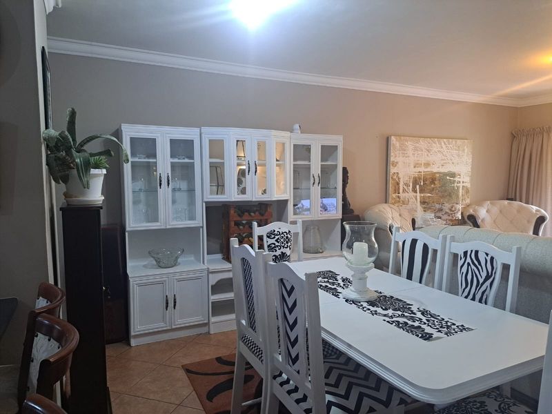 A dining area featuring tiled flooring and crown molding, currently furnished with a dining set and built-in display cabinetry.