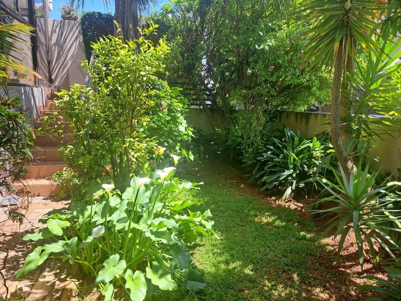 A lush, private garden area featuring established greenery, mature trees, and a tiled staircase leading to an elevated section of the property.