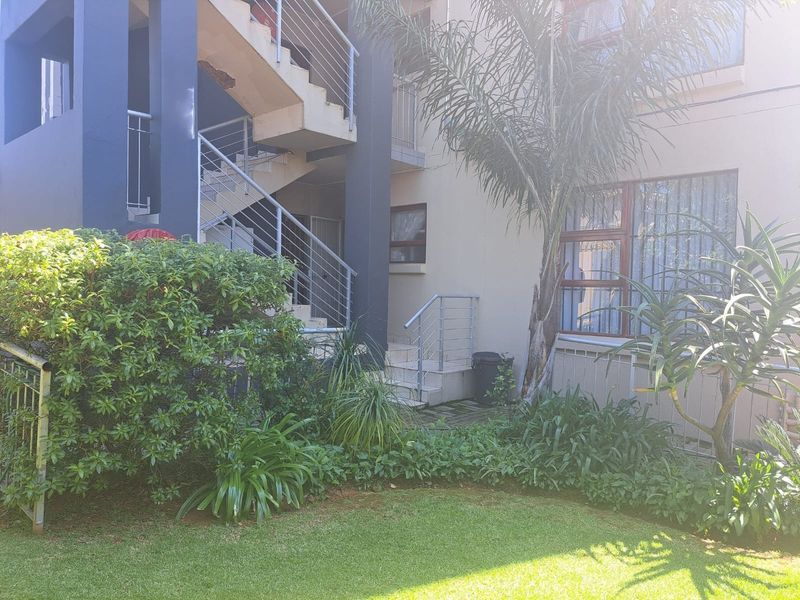 Exterior view of an apartment building featuring a staircase, metal balustrades, and a well-maintained garden area.