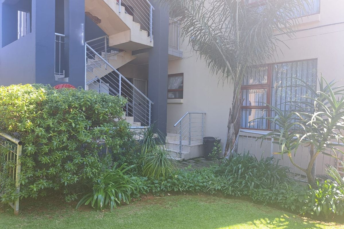 Exterior view of an apartment building featuring a staircase, metal balustrades, and a well-maintained garden area.
