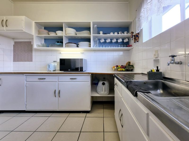 A functional kitchen featuring white built-in cabinetry, open shelving, tiled backsplash, and a stainless steel sink with tiled flooring.